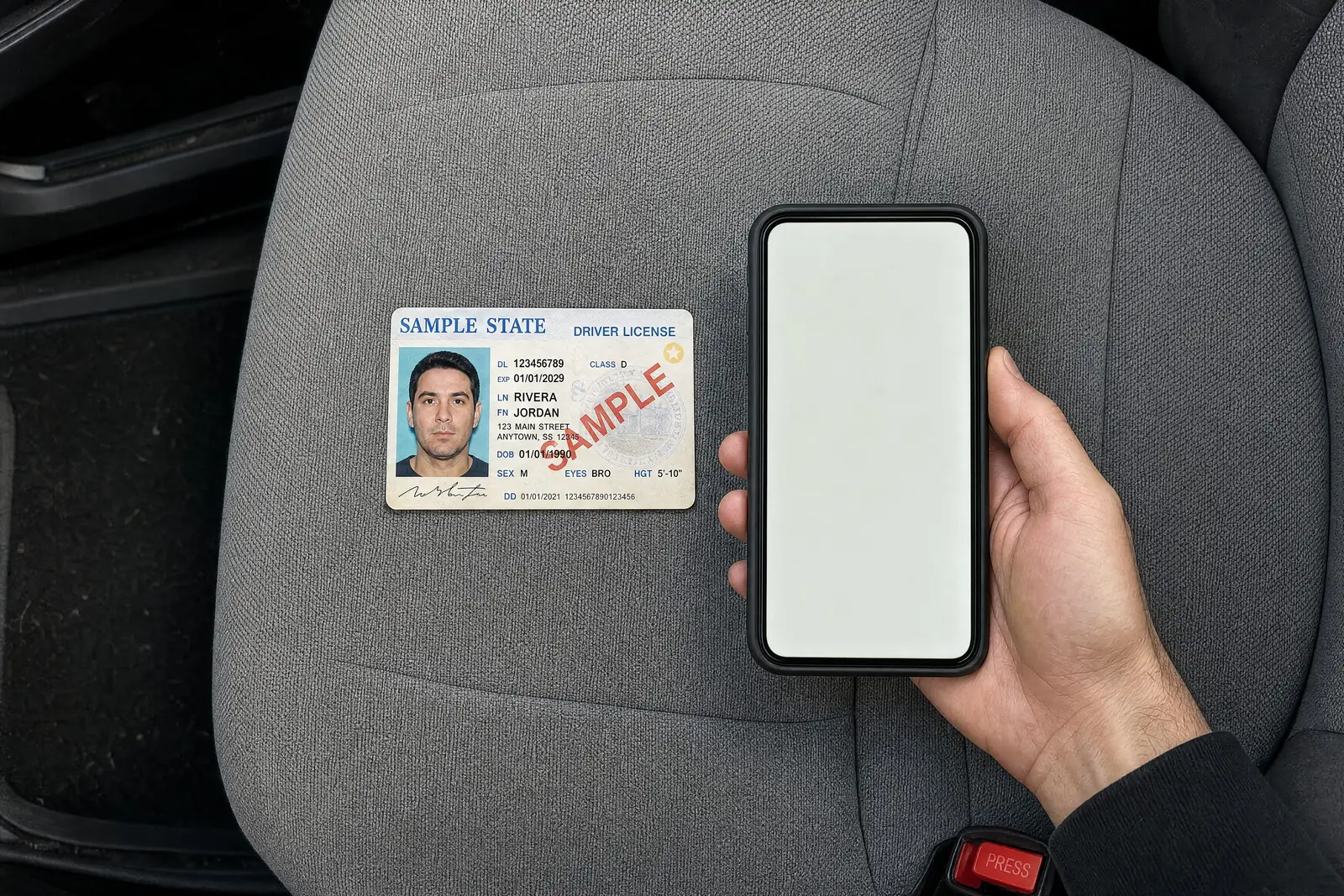 A sample driver's license on a car seat, next to a hand holding a phone.